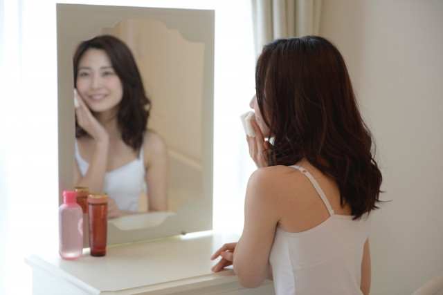 ドレッサーの鏡でラメラ構造100％の保湿化粧品をつける女性